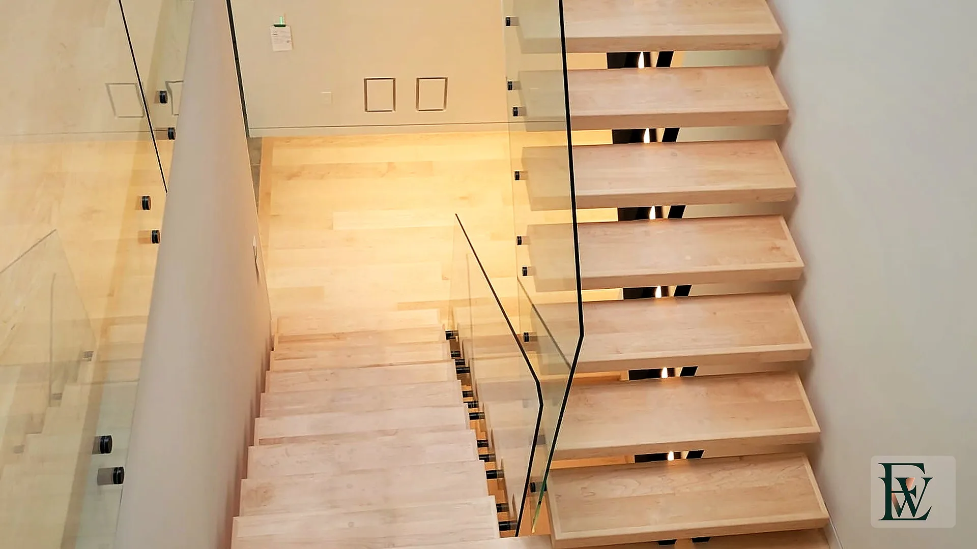 Open-riser hard maple treads with black steel stringer seen through tempered glass.