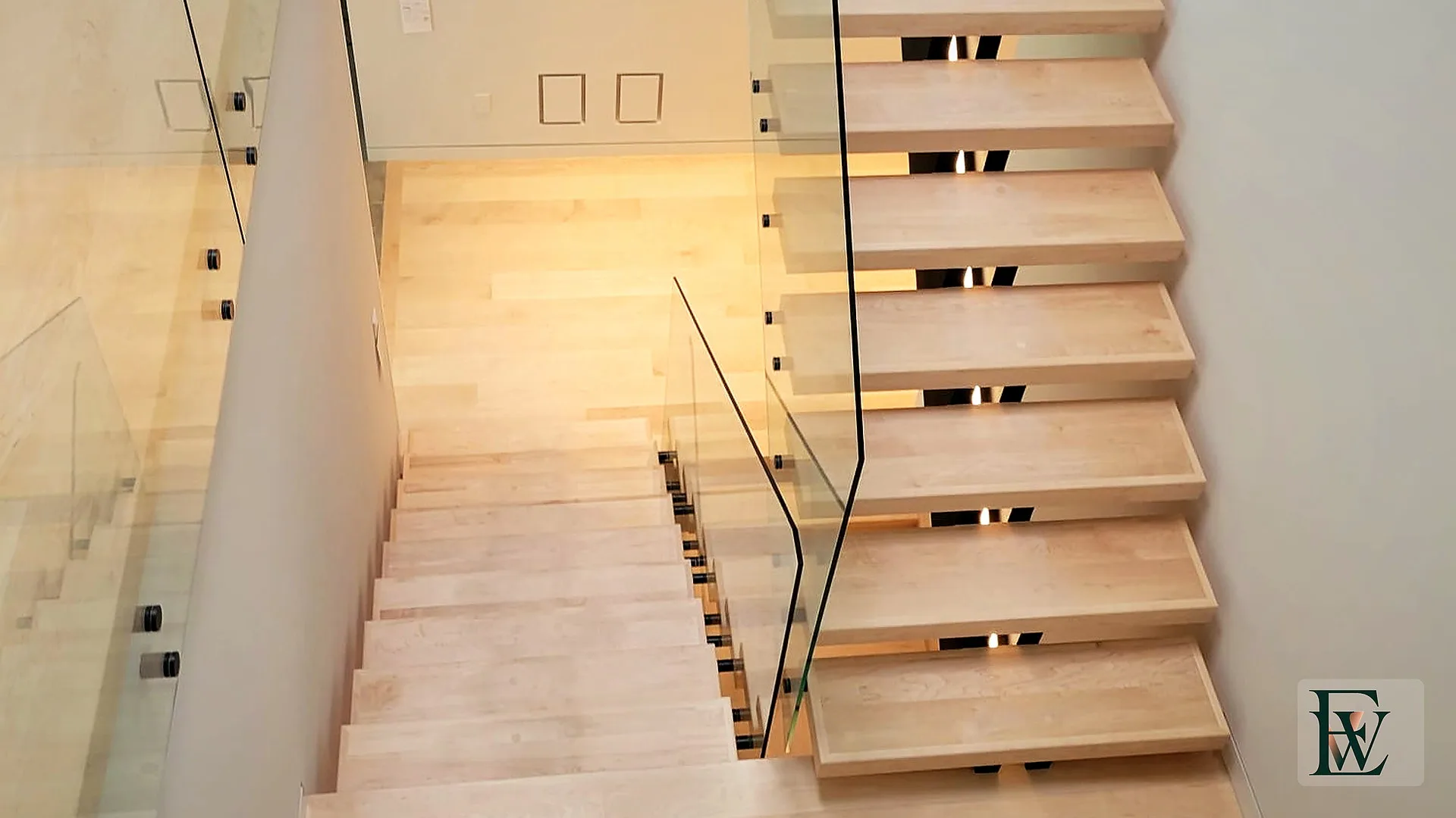 Looking down a three-level maple stair well with glass guards and matching landings.
