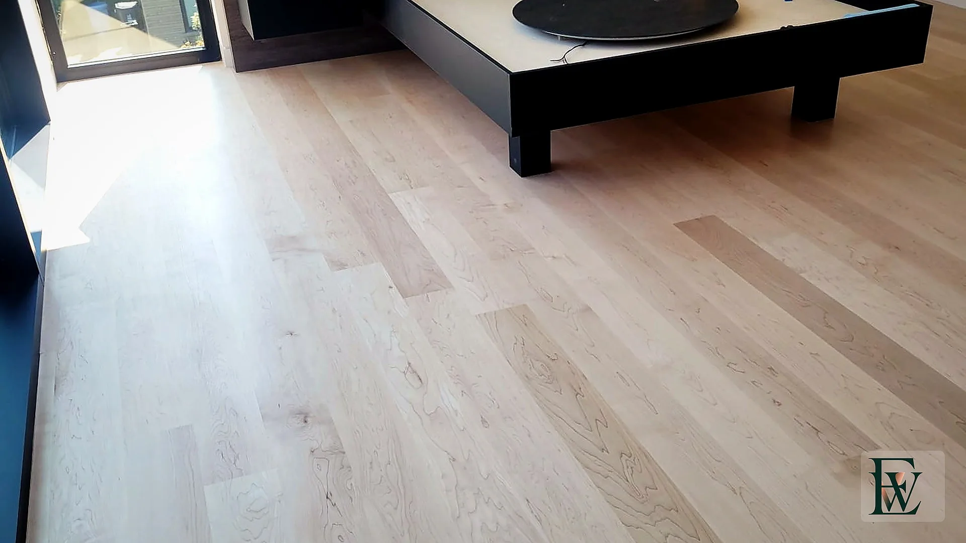 Wide hard maple planks running the length of a primary bedroom toward a floor-to-ceiling window.