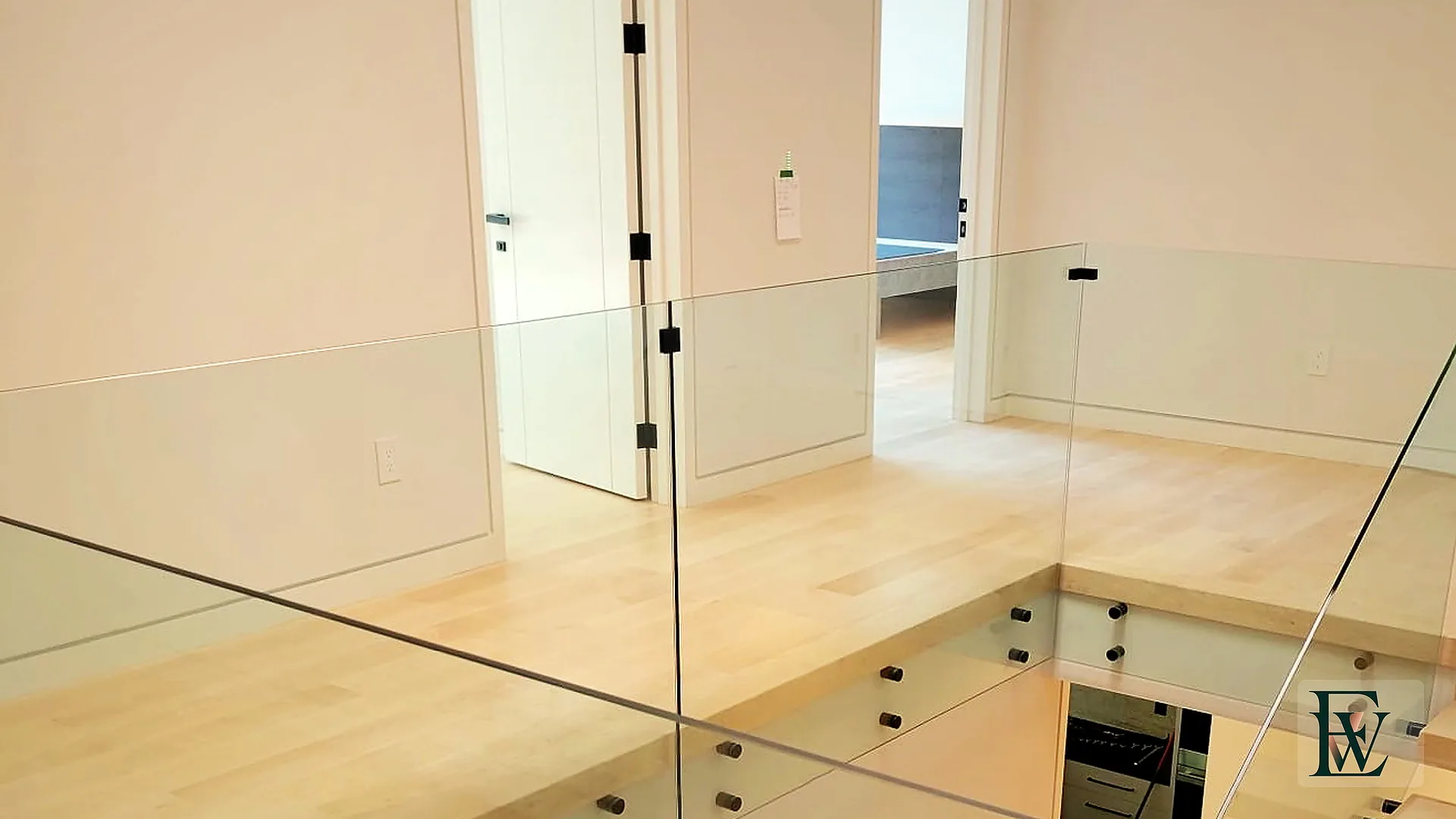 Upper-level maple landing with frameless glass guard looking into the stair void.