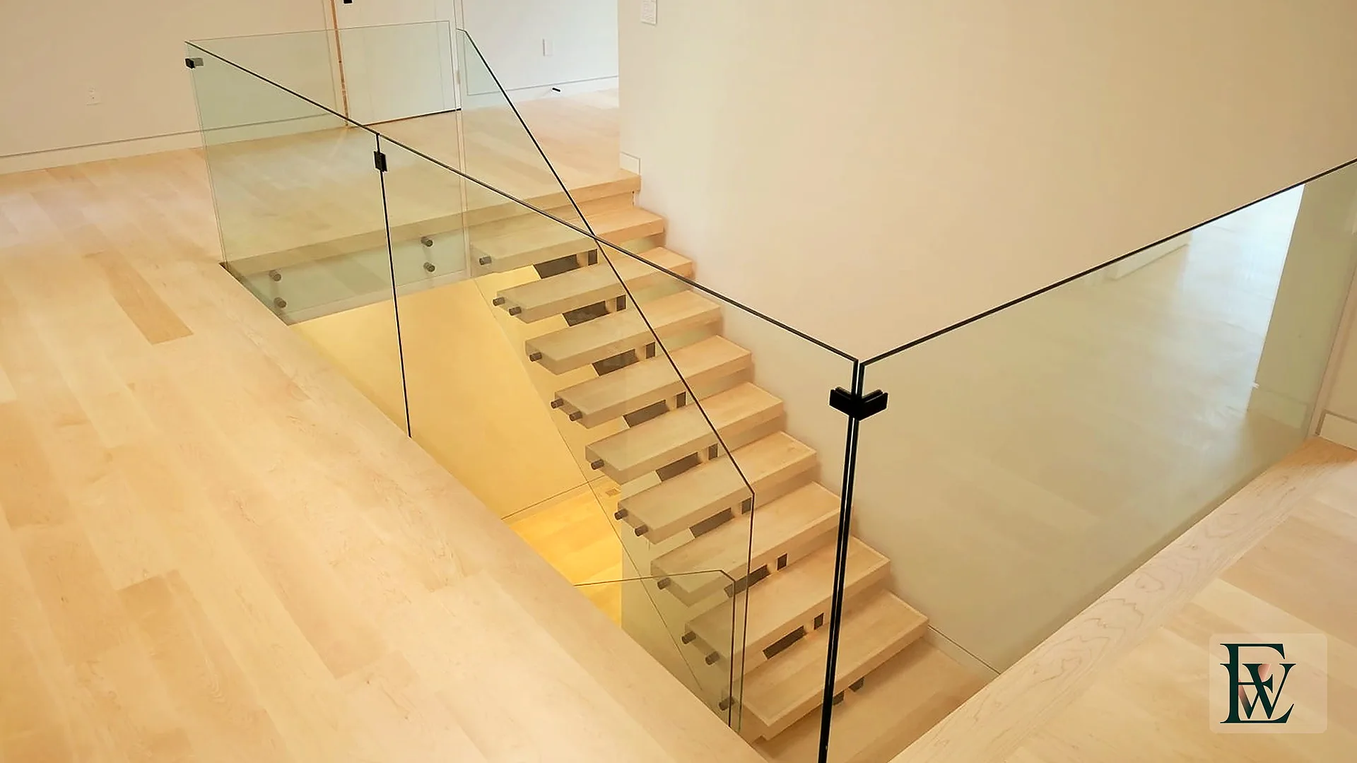 Maple floor opening to a glass-lined stair with matching open-riser treads.