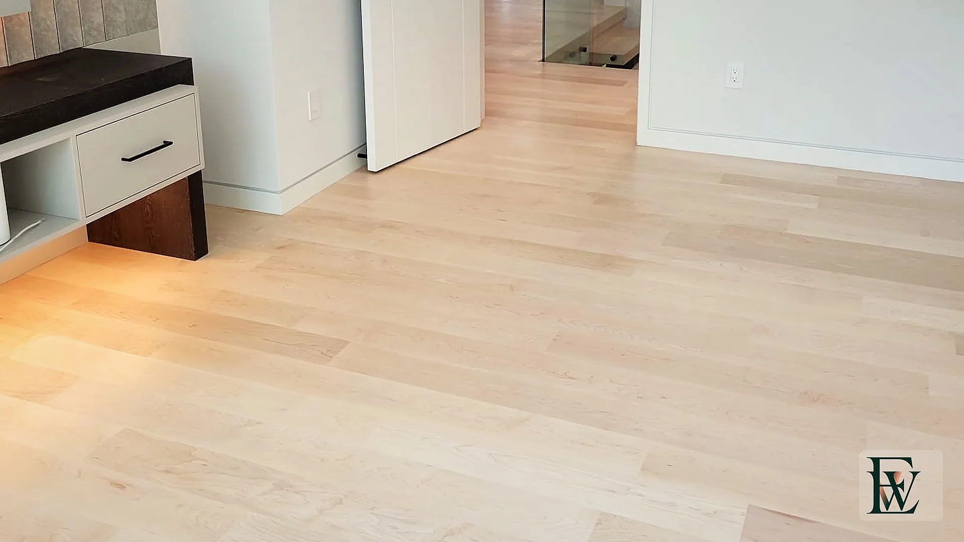Maple floor running from the primary suite through a door opening toward the glass stair.