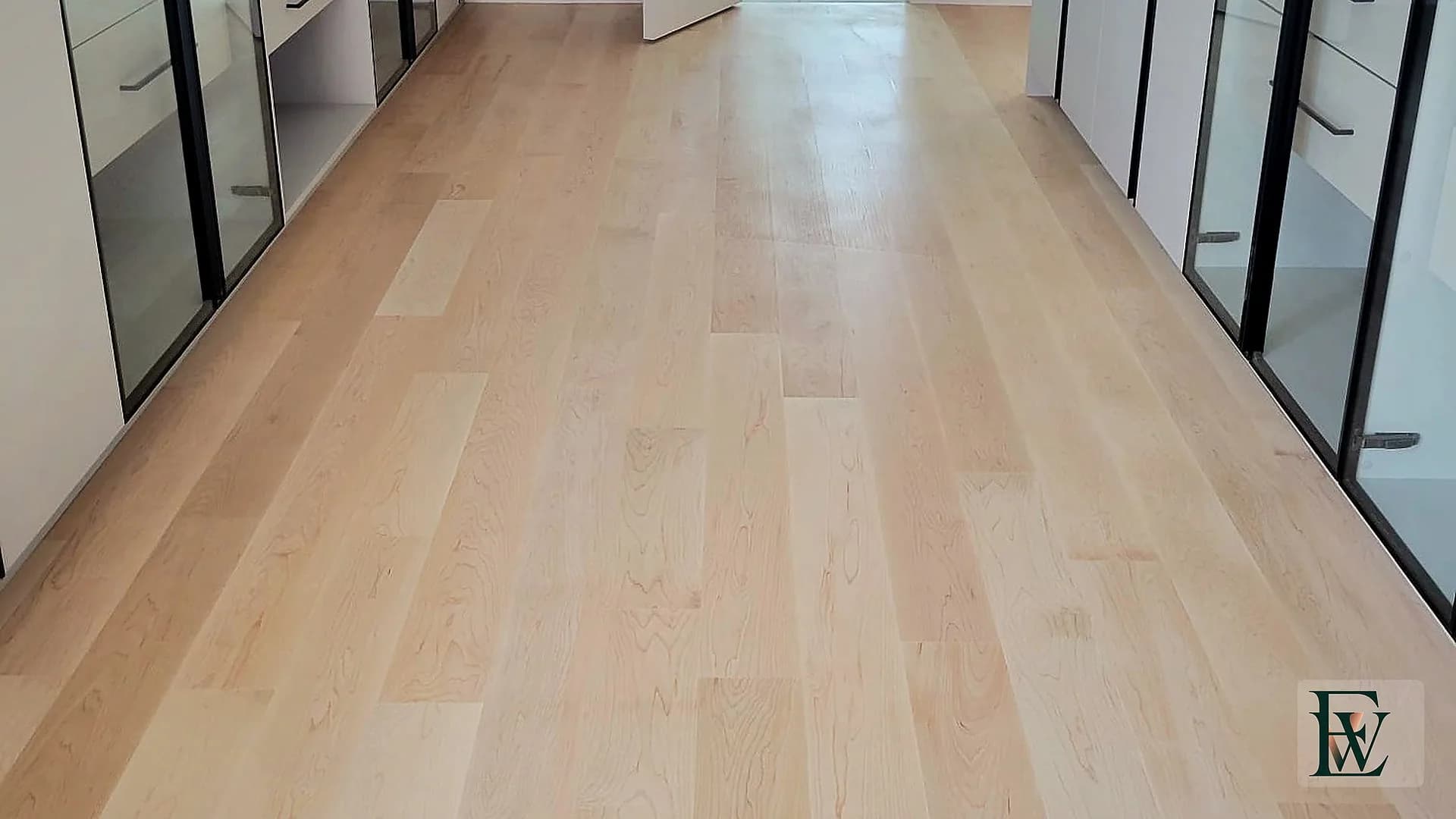 Long dressing corridor with glass wardrobe doors over a continuous hard maple floor.