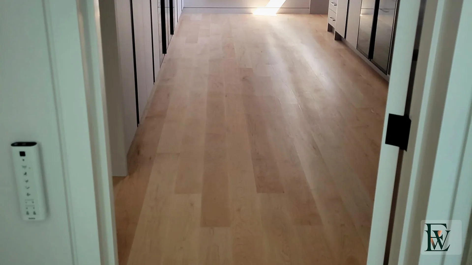 Axis view of a dressing room with maple floor, tall millwork and a window of light at the end.