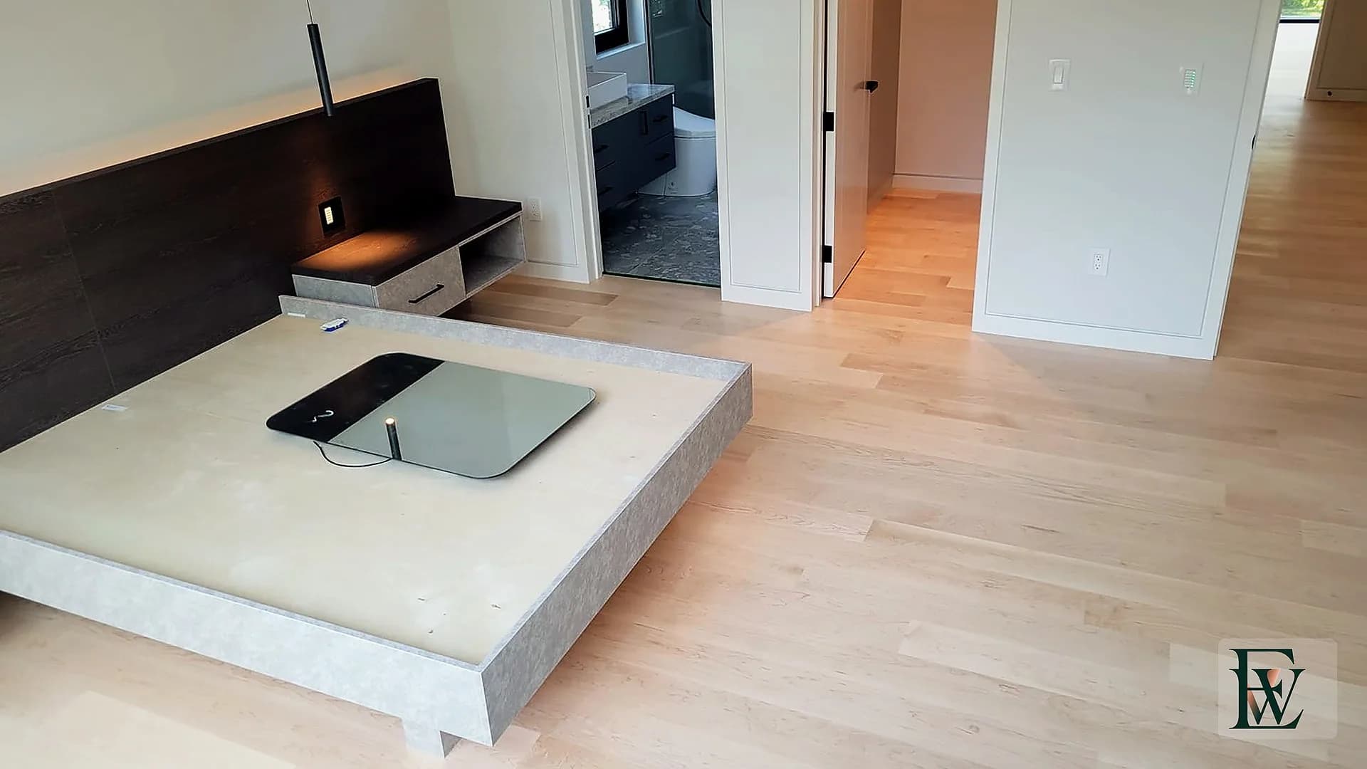 Maple bedroom floor leading past a platform bed toward an ensuite and hall.