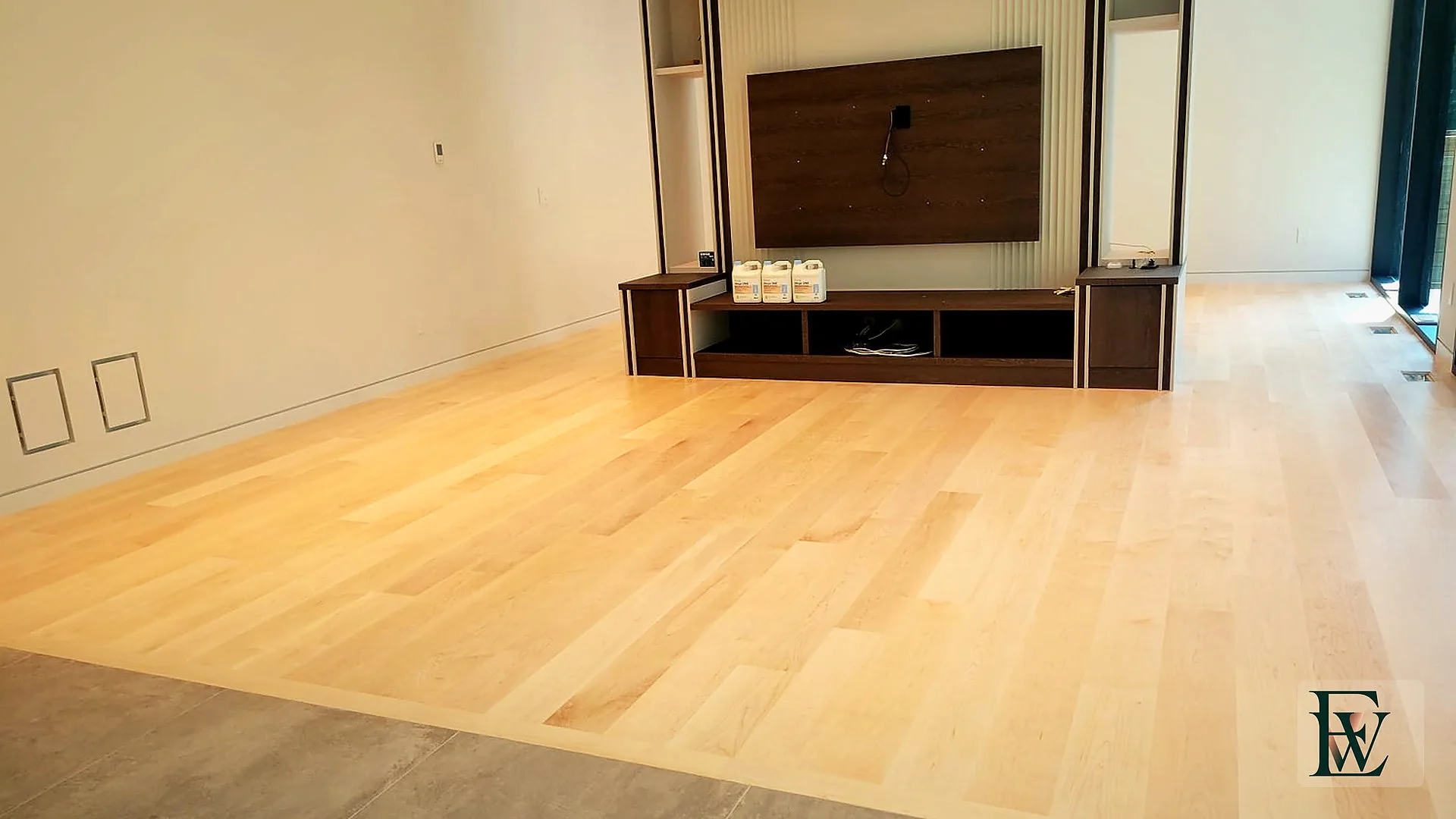 Open living room with hard maple planks running to a walnut media wall and a stone-tile threshold.