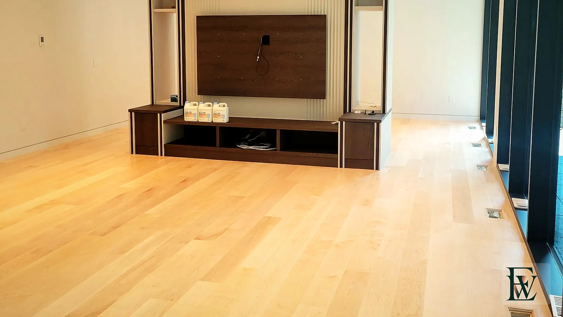 Maple living-room floor under linear ceiling lights with walnut media millwork.