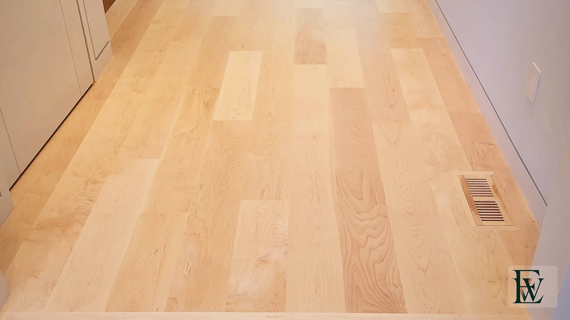 Flush maple-to-stone threshold in a hall, with maple continuing toward the stair and kitchen.