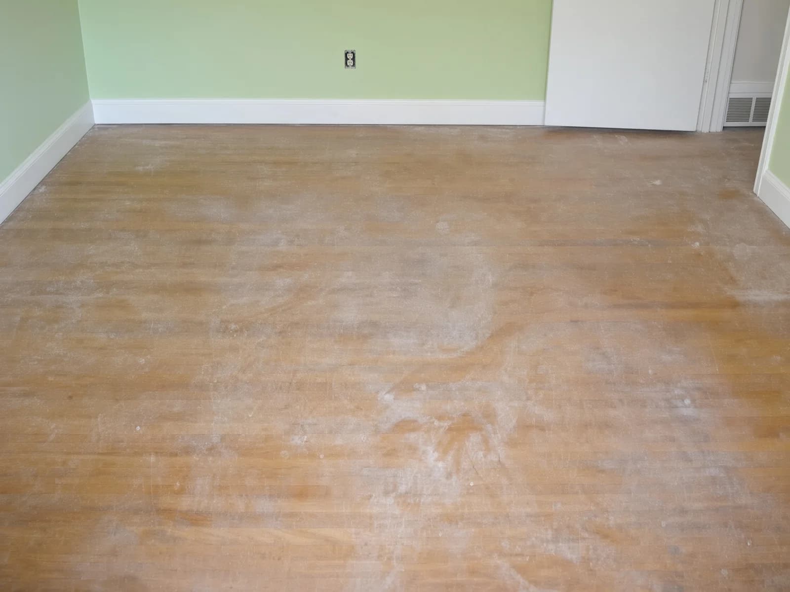 A sage-walled room with a worn, hazed floor, scratches and traffic paths visible through the old finish.