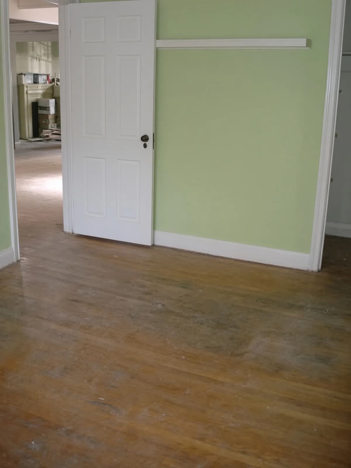 The same sage room seen through an open door, the tired floor continuing past the threshold.