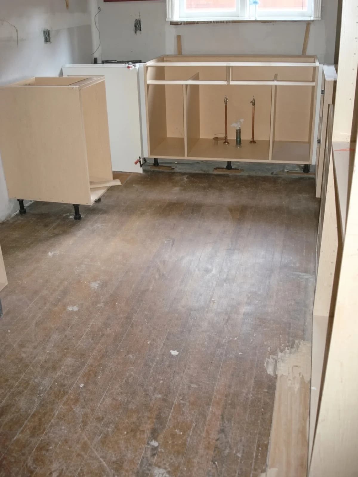 A dusty kitchen floor before the cabinets arrive, the old finish worn through in the high-traffic path.