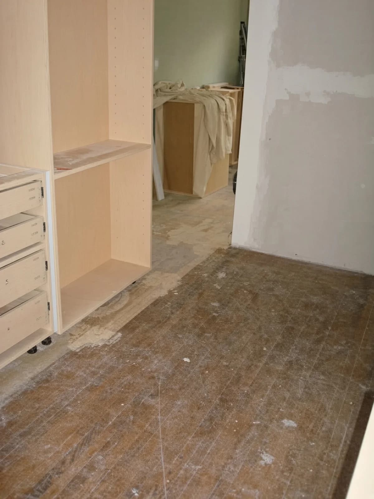 Cabinet boxes already set on an unfinished kitchen floor, ahead of the refinish.