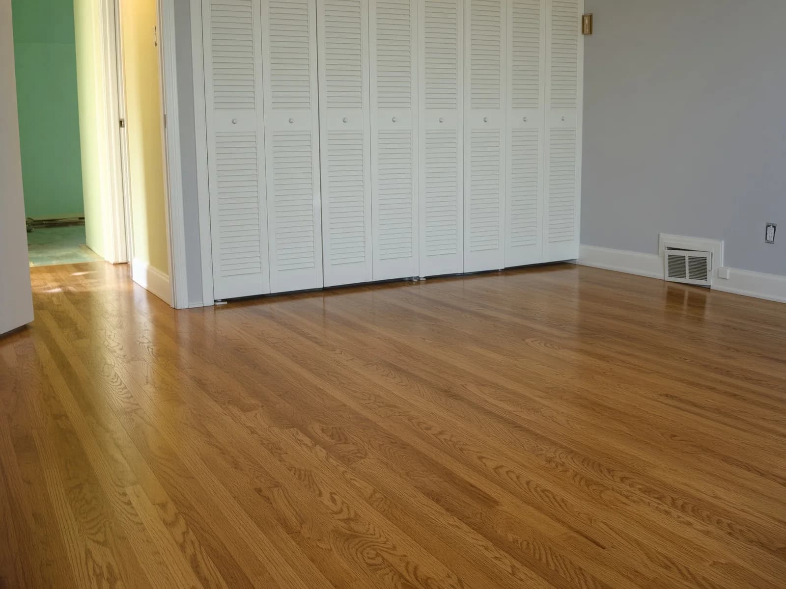 Louvered closets in a grey room, the finished floor running continuously beneath the storage wall.