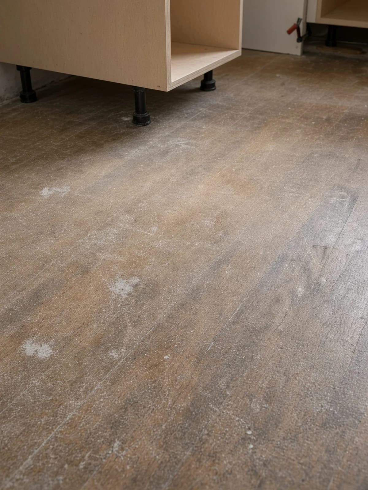 Dusty kitchen boards under the feet of cabinets that arrived before the floor was refinished.